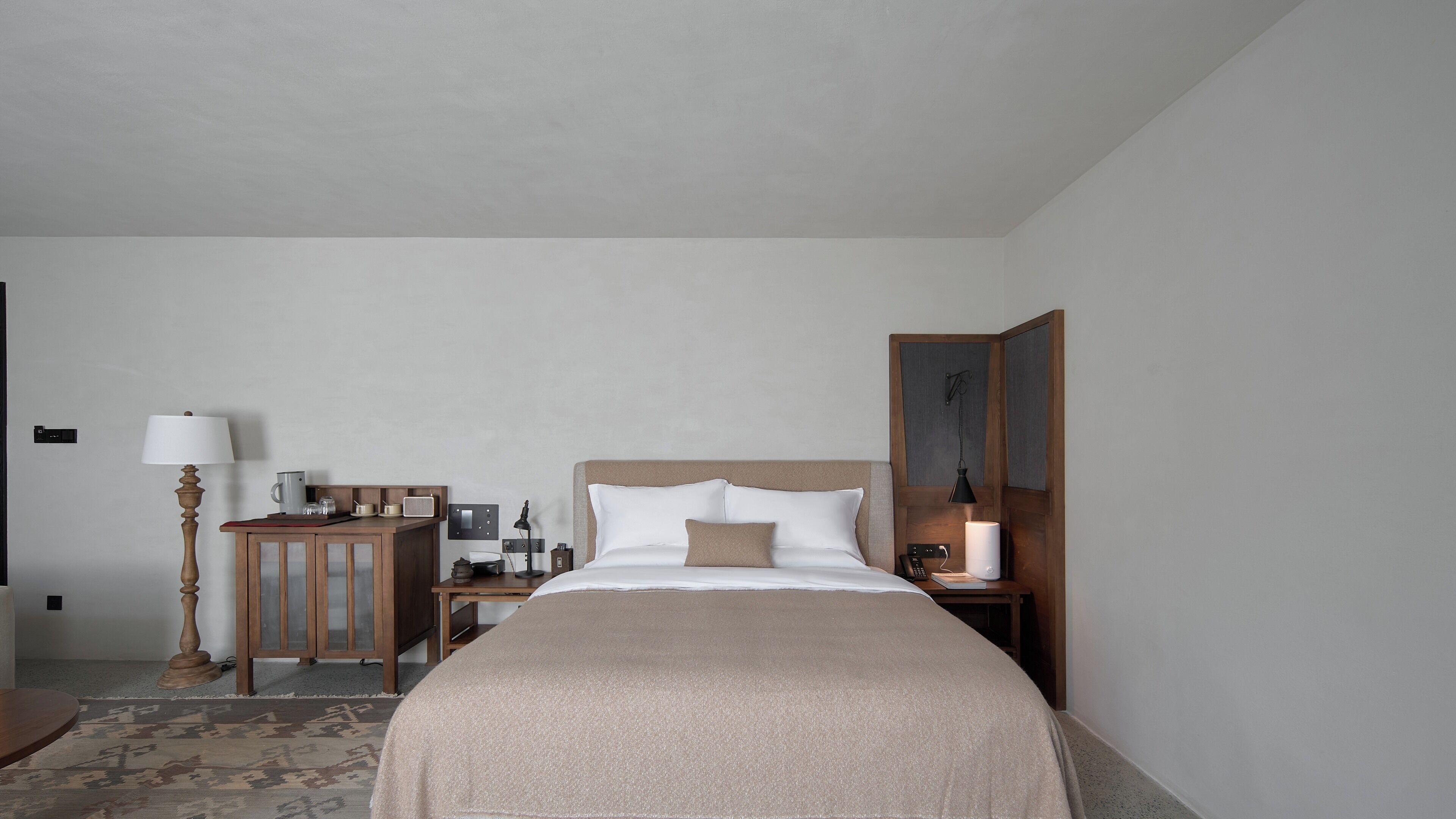 A hotel room with a bed, bedside tables, a lamp, a small cabinet, and a desk with a chair.