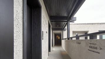 Un pasillo con pared de concreto y techo de madera, que lleva a una puerta. Hay un cartel con texto y una flecha señalando a la derecha.