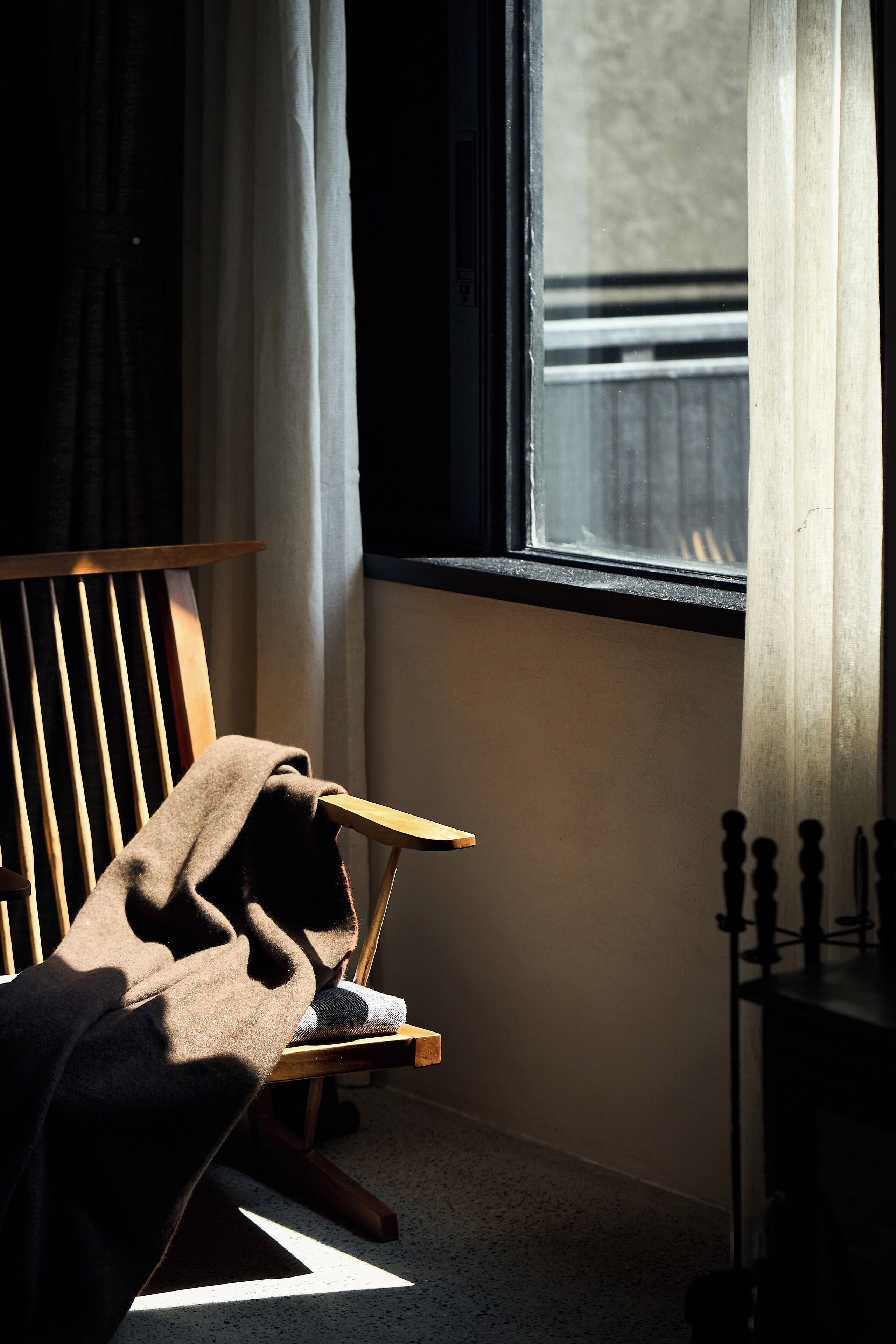 Una silla con una manta, una ventana con cortinas y un radiador.