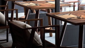 Een restaurant interieur met houten tafels en stoelen, grote ramen en een modern design.