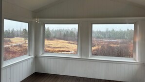 A room with three large windows offering views of a forested landscape.