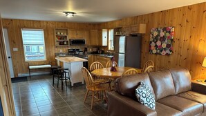A cozy kitchen with wooden cabinets, a dining table with chairs, and a brown leather sofa.