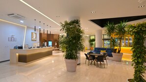 Um saguão moderno de hotel com balcão de recepção, área de estar e plantas em vasos.