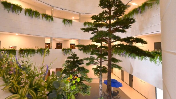Um átrio com vários níveis, plantas internas, uma árvore central e áreas de estar.