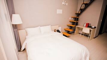 A hotel room with a bed, a desk, a chair, a lamp, a staircase, and a wall-mounted light switch.