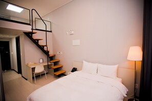 Une chambre d’hôtel équipée d’un lit, d’un bureau, d’une chaise, d’un téléphone, d’une lampe et d’un escalier.