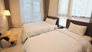 Quarto de hotel com duas camas, mesa de cabeceira, abajur e janela com cortinas.