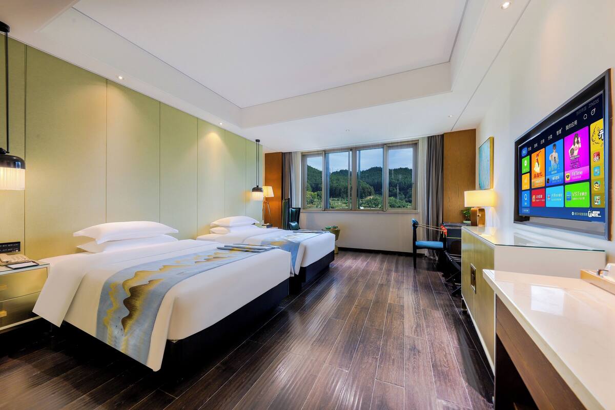 Une chambre d’hôtel avec un grand lit, un bureau, une télévision et une fenêtre donnant sur l’extérieur.
