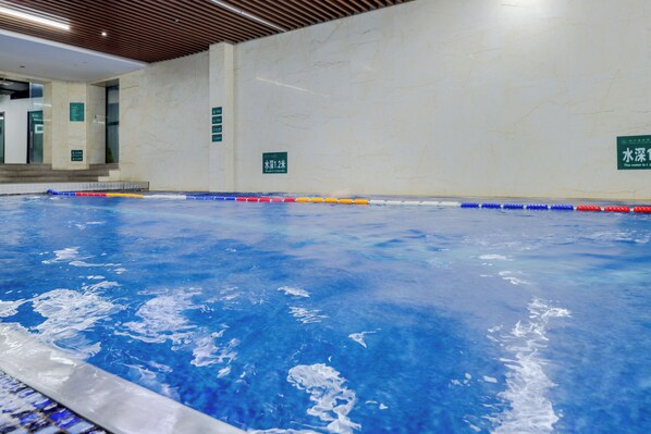 Une piscine à l’eau d’un bleu cristallin, entourée d’une terrasse carrelée et surmontée d’un plafond en bois.