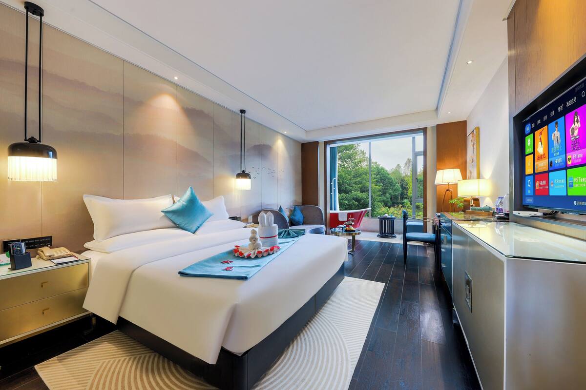 Une chambre d’hôtel moderne, dotée d’un grand lit, de tables de chevet, d’un bureau et d’une télévision.