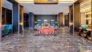 Eine großzügige Lobby mit Marmorboden, einer zentralen Sitzgruppe mit Tisch und Stühlen sowie großen Fenstern mit Blick auf die Stadt.
