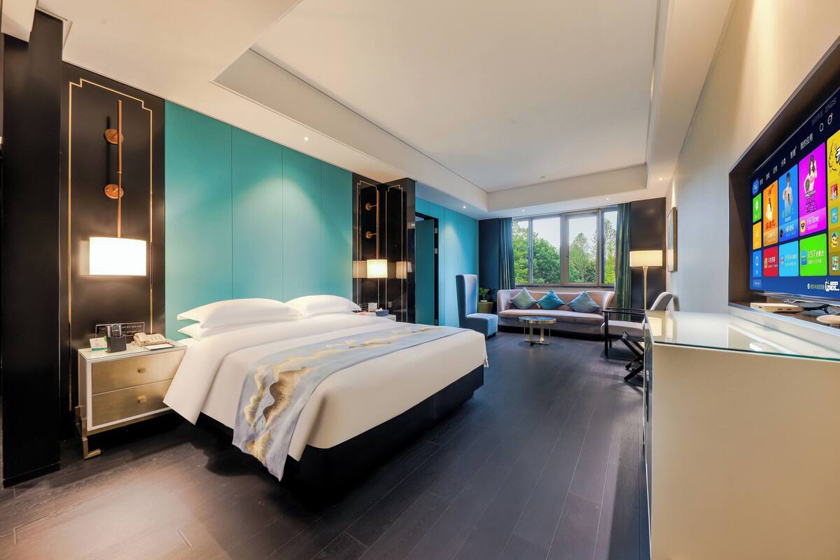 Une chambre d’hôtel moderne avec un grand lit, un bureau et un téléviseur diffusant des programmes aux couleurs vives.
