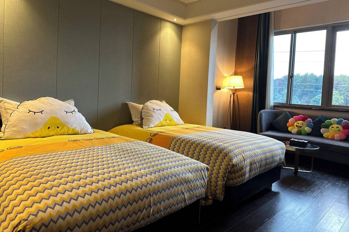 Une chambre d’hôtel avec deux lits, un canapé, une lampe et une vue sur les arbres par la fenêtre.