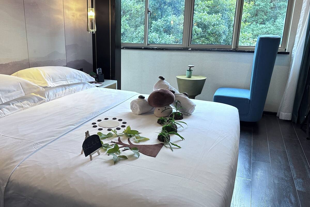 Un lit bien fait, avec du linge de lit blanc, une petite décoration en forme d’arbre et un ours en peluche posé sur le lit.