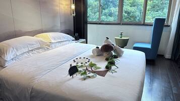 Een net opgemaakt bed met witte lakens, een kleine boomdecoratie en een teddybeer.