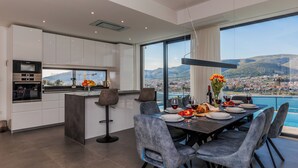 A modern kitchen with a dining area, large windows with a view of the city and mountains, and a table set for a meal.