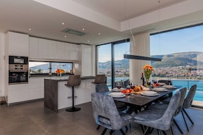 A modern kitchen with a dining area, large windows with a view of the city and mountains, and a table set for a meal.