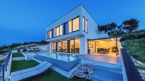 A modern two-story house with a swimming pool, outdoor seating, and a well-maintained garden.