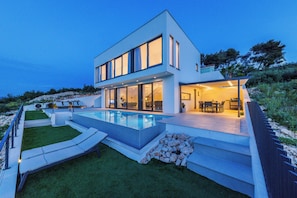 A modern two-story house with a swimming pool, outdoor seating, and a well-maintained garden.