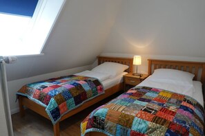 Ein Zimmer mit zwei Betten, jedes mit einer farbenfrohen Stegdecke, einem Nachttisch mit Lampe und einem Fenster mit Blick auf den Himmel.