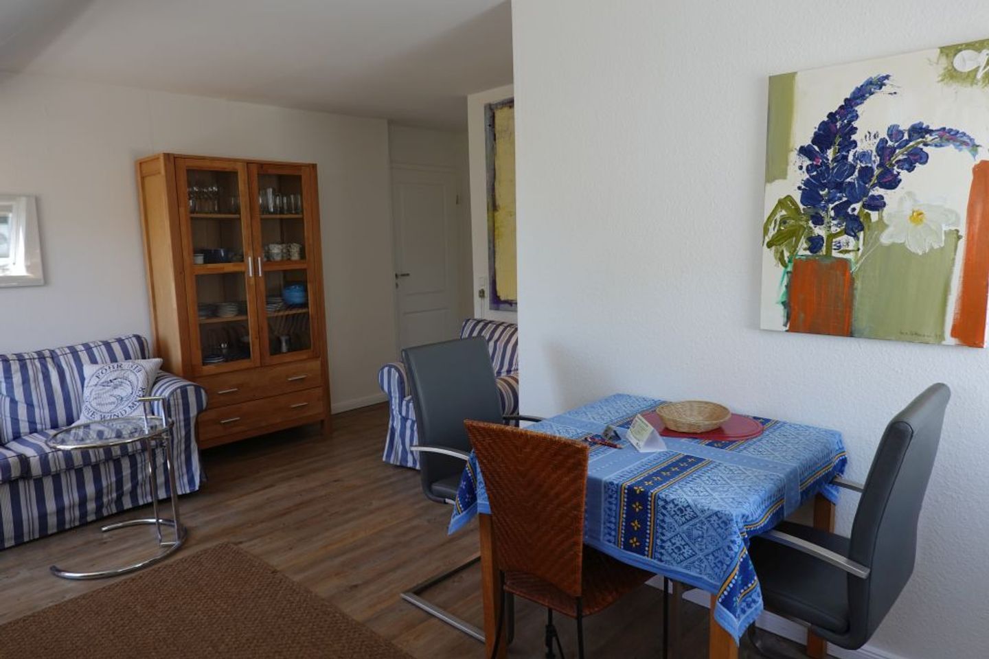 A living room with a striped sofa, a wooden cabinet, and a dining table with chairs.