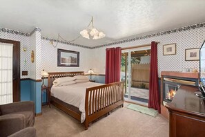 Un dormitorio con cama, mesitas de noche, escritorio, chimenea y vistas al jardín a través de una puerta corrediza.