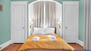 A hotel room with a bed, two white doors, a white arched headboard, and two bedside lamps. - Lakeside Vintage Retreat | Classic RVA Charm (Henrico)