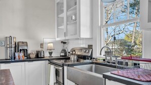 A modern kitchen with white cabinetry, stainless steel appliances, a large window, and a view of trees. - Lakeside Vintage Retreat | Classic RVA Charm (Henrico)