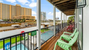 A balcony with a view of a swimming pool, a parking area, and high-rise buildings in the background.