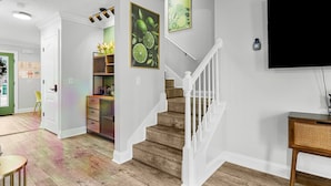 A modern interior with a staircase, a flat-screen TV mounted on the wall, and a bookshelf with decorative items.