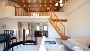 Ein großzügiger Wohnbereich mit hoher Decke, einer Holztreppe und einer modernen Küche im Hintergrund.