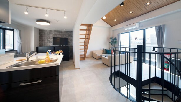 Eine moderne Küche mit eingebautem Ofen, ein Essbereich mit Tisch und Stühlen, eine Treppe, die zu einer oberen Ebene führt, und große Fenster, die für natürliches Licht sorgen.