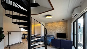 Ein modernes Interieur mit einer Wendeltreppe, einer Steinwand, einem Flachbildfernseher und einem großen Fenster mit Stadtblick.