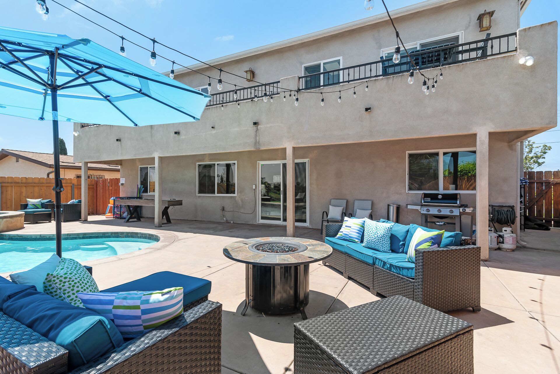 A backyard with a swimming pool, outdoor furniture, a barbecue grill, and a pergola with string lights.