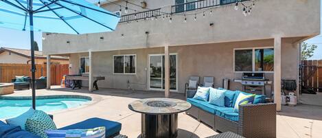 A backyard with a swimming pool, outdoor furniture, a barbecue grill, and a pergola with string lights.