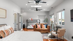 A modern bedroom with a large bed, a sofa, a desk, and a ceiling fan. - New! Spacious 5BD Home with Games, Pool & Hot Tub! (San Diego)