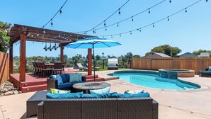 A backyard with a swimming pool, outdoor furniture, and string lights. - New! Spacious 5BD Home with Games, Pool & Hot Tub! (San Diego)