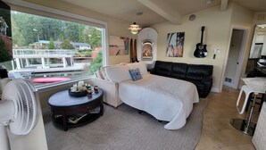 A living room with a view of a dock and boats, a fireplace, a guitar, and a fan. - Unique Lake Goodwin Waterfront Cabin with Private Hot Tub and Boat Moorage (Stanwood)