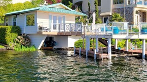 A houseboat with a deck and outdoor seating, connected to a dock. - Unique Lake Goodwin Waterfront Cabin with Private Hot Tub and Boat Moorage (Stanwood)