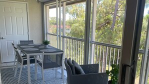 Un balcon ensoleillé avec une table et des chaises, un ventilateur de plafond et une vue sur les arbres.
