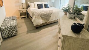 Une chambre à coucher comprenant un lit, des tables de chevet, un miroir, un ventilateur de plafond et un petit banc.