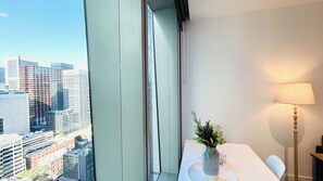 Enjoy a panoramic city view from the comfort of this stylish room, featuring a dining table, floor lamp, and lush greenery.
