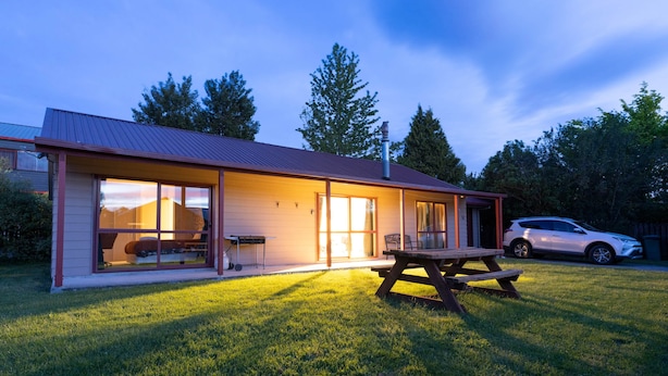 A modern house with a large glass window, a wooden deck, and a white car parked outside. - Cozy | Functional | Private - HS65214 (Hanmer Springs)