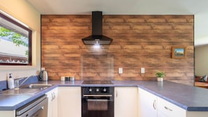A kitchen with a wooden backsplash, a built-in oven, and a window with a view of trees. - Cozy | Functional | Private - HS65214 (Hanmer Springs)