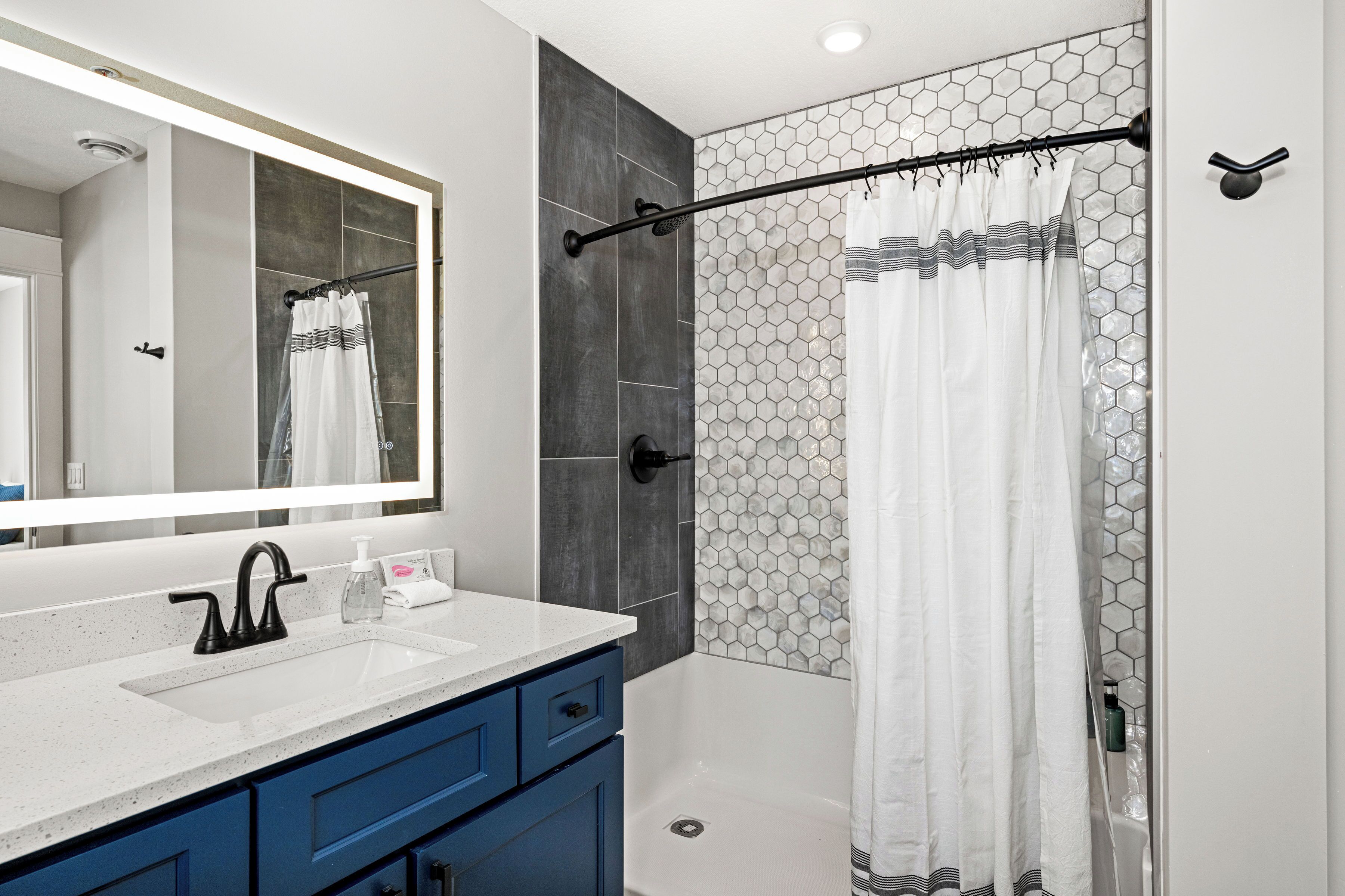 A modern bathroom with a white sink, blue cabinets, a large mirror, and a shower with a hexagonal tile pattern.
