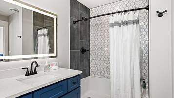 A modern bathroom with a white sink, blue cabinets, a large mirror, and a shower with a hexagonal tile pattern.