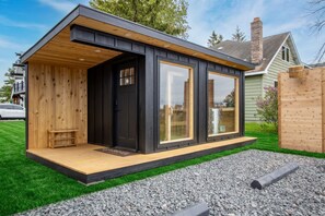 Un bâtiment moderne, de plain-pied, doté d’une terrasse en bois, de grandes fenêtres et d’une façade noire.