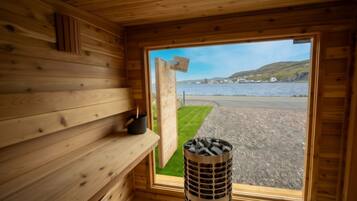 A wooden cabin with a window overlooking a beach and water.