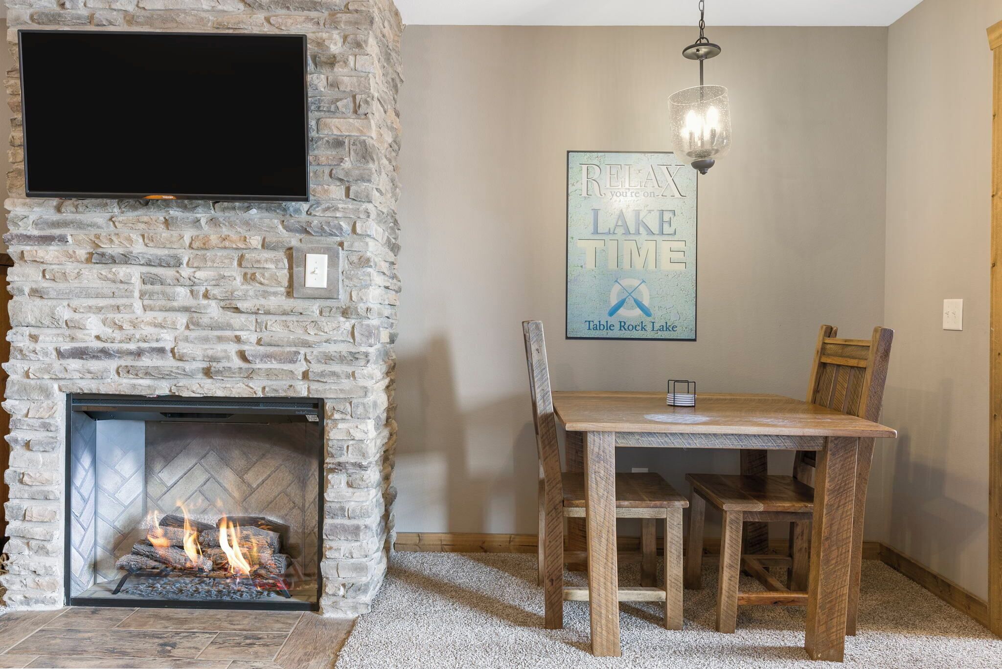 A stone fireplace with a TV mounted above it, a table with chairs, and a 'Relax Lake Time' sign on the wall.