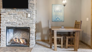 Una chimenea de piedra con un televisor montado encima, una mesa con sillas, y un cartel en la pared que dice 'Relax Lake Time'.